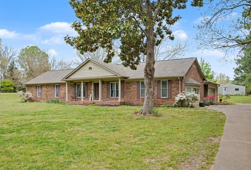 View of front facade with a front lawn, covered porch, roof with shingles, and brick siding