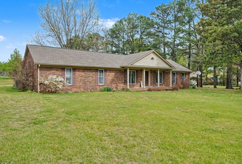 Ranch-style house featuring covered porch, a front lawn, a shingled roof, and brick siding
