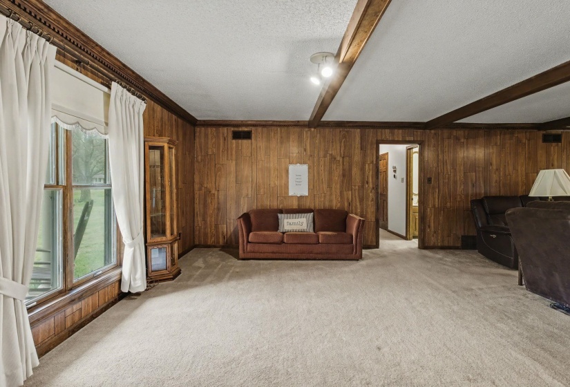 Carpeted living area featuring beamed ceiling, a textured ceiling, and wooden walls