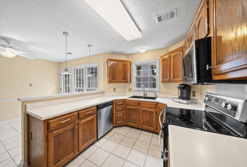 Kitchen featuring stainless steel appliances, light tile patterned flooring, a peninsula, brown cabinets, and a textured ceiling