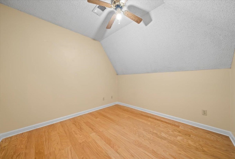 Bonus room with a textured ceiling, lofted ceiling, wood finished floors, and a ceiling fan