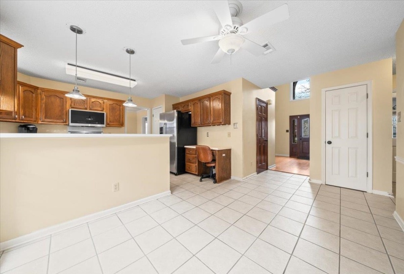 Kitchen featuring pendant lighting, stainless steel refrigerator with ice dispenser, a desk, brown cabinets, and light countertops