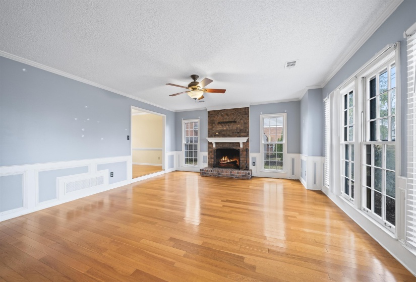 Unfurnished living room with wainscoting, a decorative wall, ornamental molding, a textured ceiling, and a fireplace