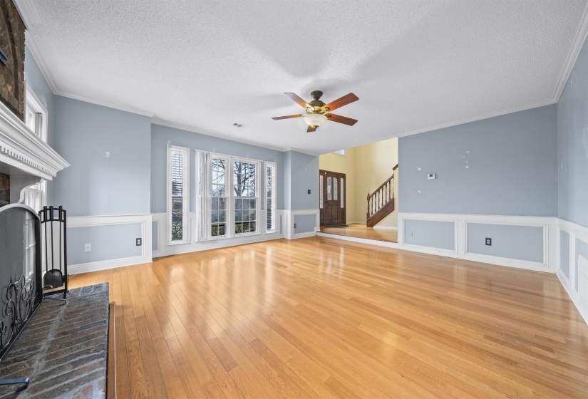 Unfurnished living room featuring a brick fireplace, a textured ceiling, light wood-style flooring, stairs, and ornamental molding