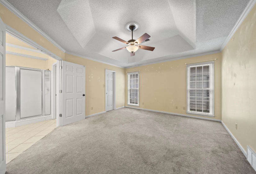 Unfurnished bedroom featuring crown molding, a tray ceiling, a textured ceiling, ceiling fan, and light carpet