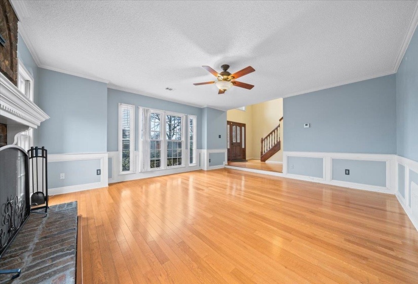 Unfurnished living room with a fireplace, a textured ceiling, light wood-style floors, ornamental molding, and a ceiling fan