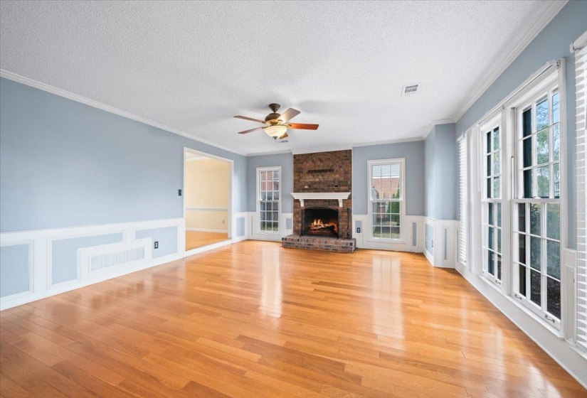 Unfurnished living room featuring wainscoting, a decorative wall, crown molding, a textured ceiling, and wood finished floors