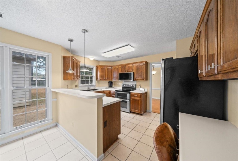 Kitchen with light countertops, a peninsula, appliances with stainless steel finishes, brown cabinetry, and light tile patterned floors