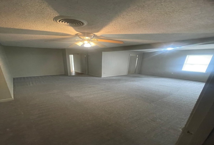 Empty room featuring a textured ceiling, carpet, and ceiling fan