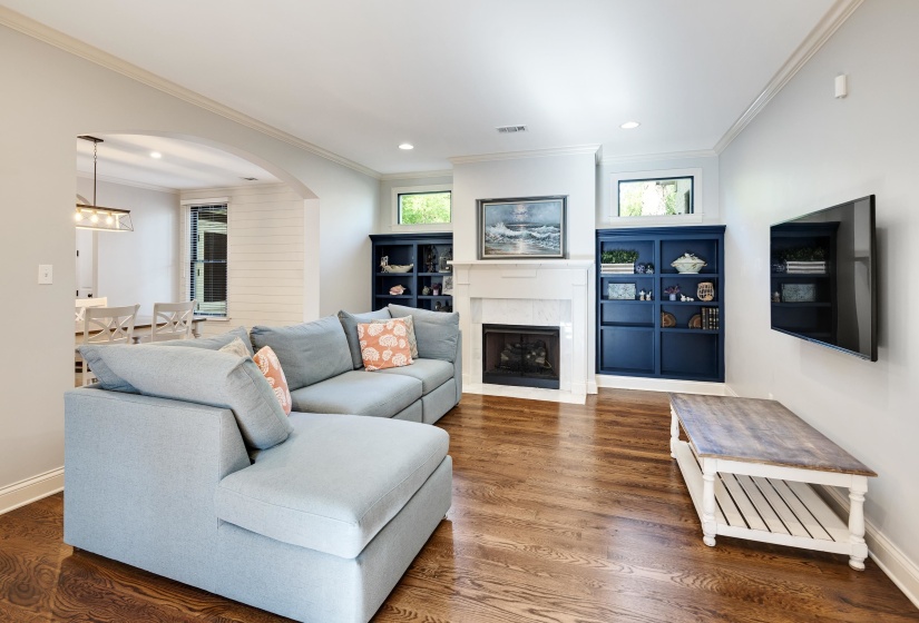 Living area with arched walkways, wood finished floors, a fireplace with flush hearth, ornamental molding, and recessed lighting