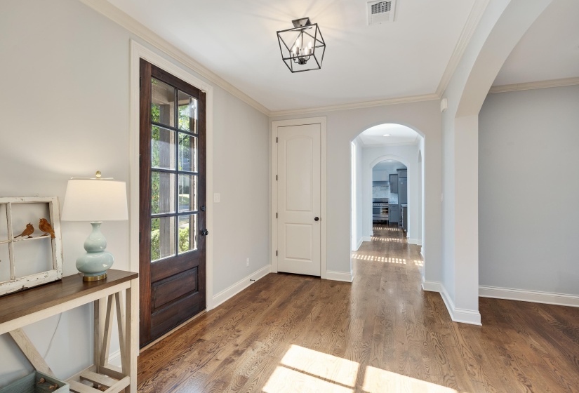 Entrance foyer with ornamental molding, arched walkways, and light wood finished floors