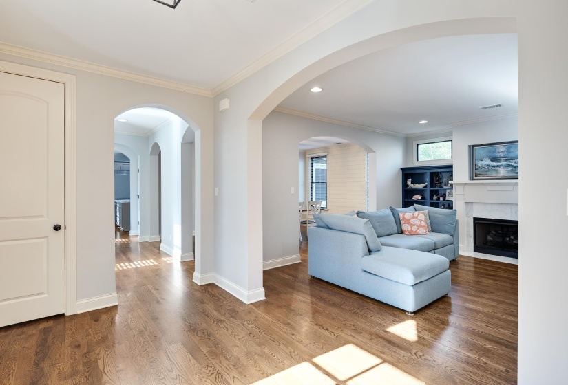 Living area with crown molding, wood finished floors, a fireplace with flush hearth, arched walkways, and recessed lighting