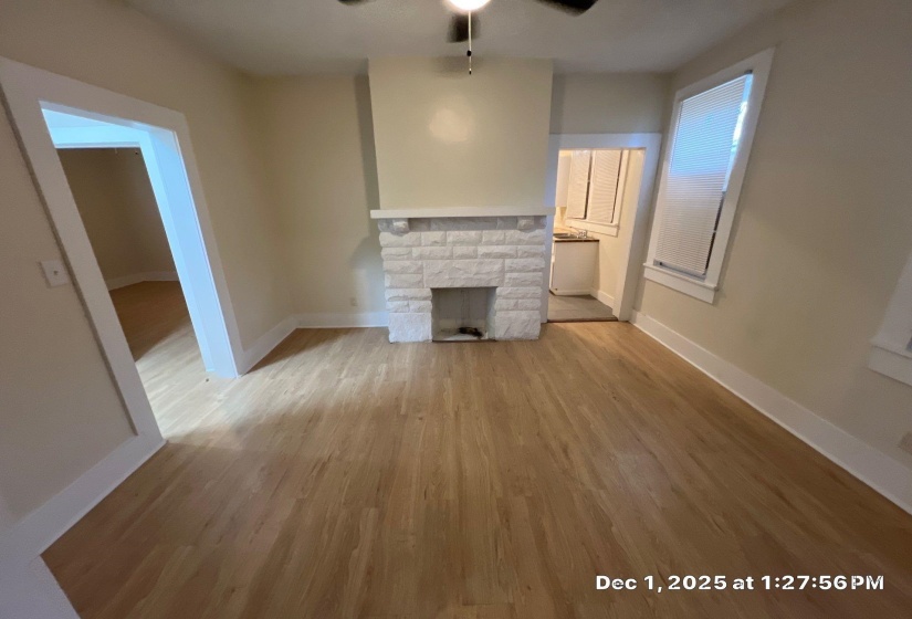 Unfurnished living room featuring light wood-style floors, a ceiling fan, and a stone fireplace