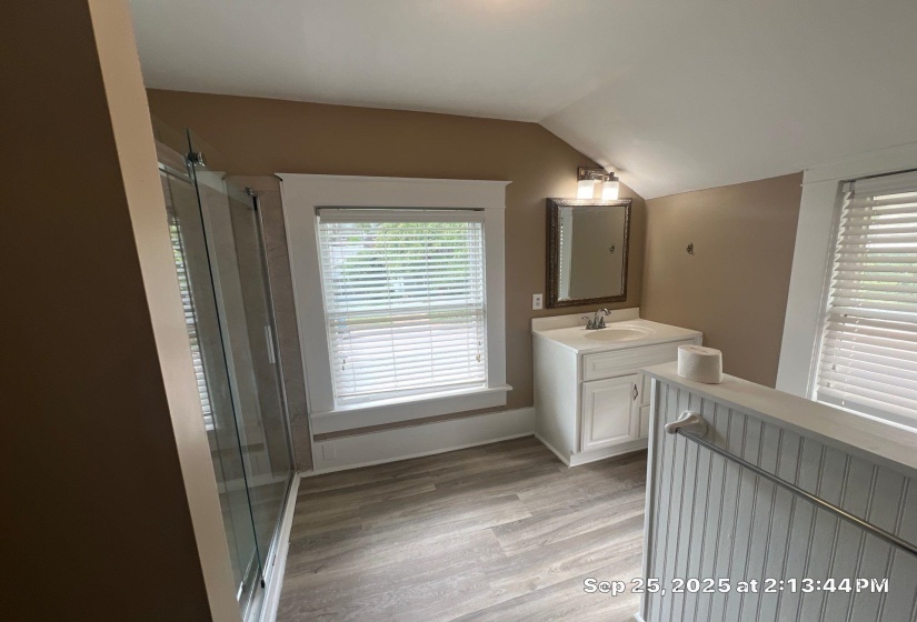 Full bath with vanity, vaulted ceiling, light wood finished floors, and a stall shower
