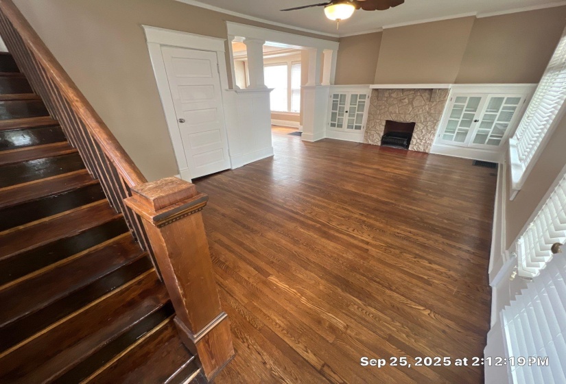 Unfurnished living room with dark wood-style floors, ceiling fan, a stone fireplace, and crown molding