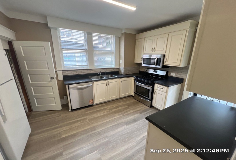Kitchen with dark countertops, stainless steel appliances, light wood-style floors, tasteful backsplash, and white cabinets