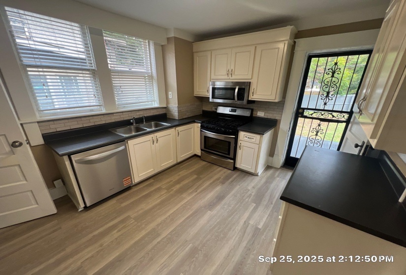 Kitchen with dark countertops, stainless steel appliances, white cabinets, backsplash, and light wood-style flooring