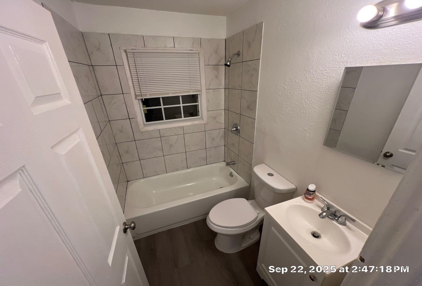 Full bath with vanity, a textured wall, shower / washtub combination, and dark wood finished floors
