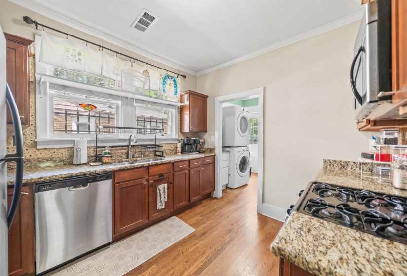 Kitchen featuring stainless steel appliances, light stone countertops, stacked washer and clothes dryer, crown molding, and light wood-style floors