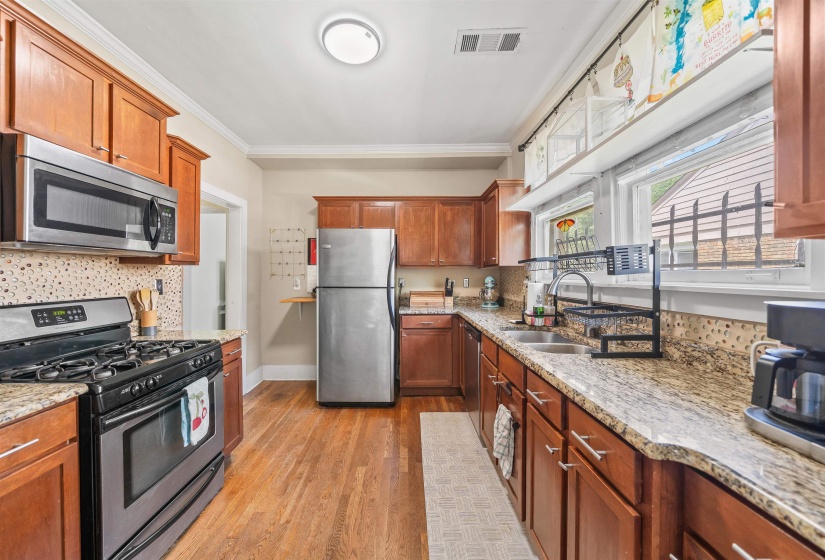 Kitchen with stainless steel appliances, light wood-style flooring, wood finish cabinets, light stone counters, and crown molding