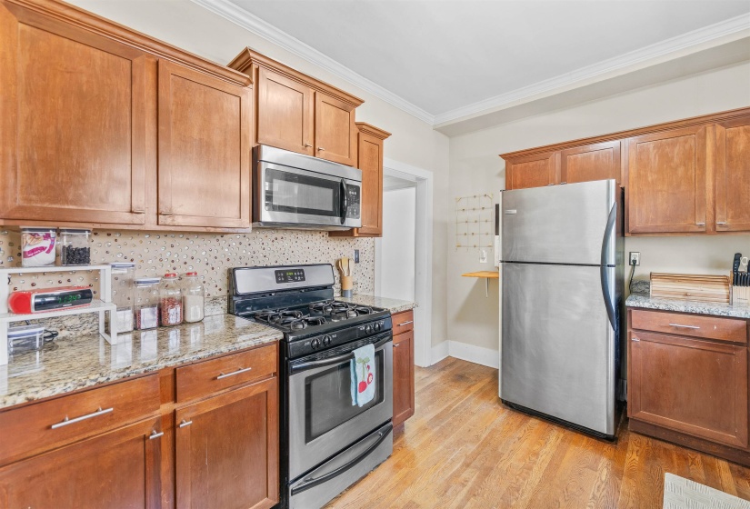 Kitchen featuring stainless steel appliances, crown molding, light stone countertops, light wood-style flooring, and wood finish cabinets