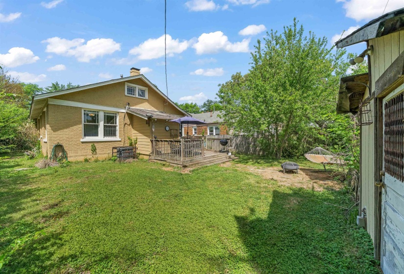 Back of house featuring a wooden deck, a lawn, an outdoor fire pit, and a chimney