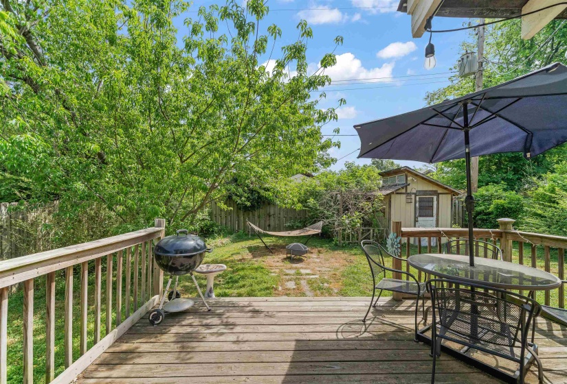 Wooden terrace featuring outdoor dining area, a fenced backyard, grilling area, and a storage unit