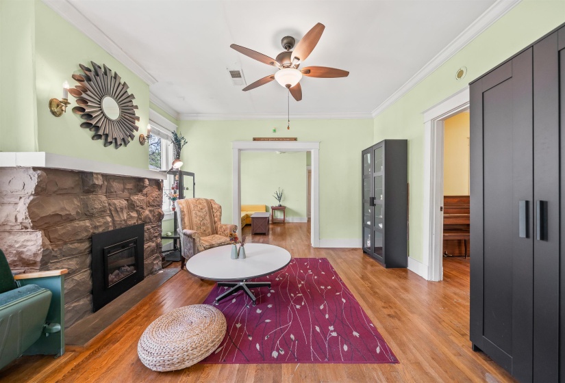 Sitting room featuring ornamental molding, a stone fireplace, a ceiling fan, and wood finished floors