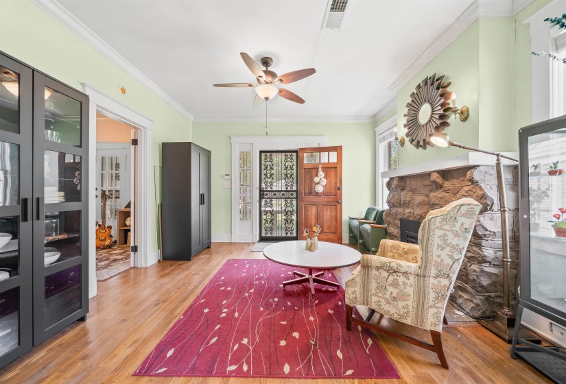 Sitting room featuring a stone fireplace, ornamental molding, light wood-style floors, and ceiling fan