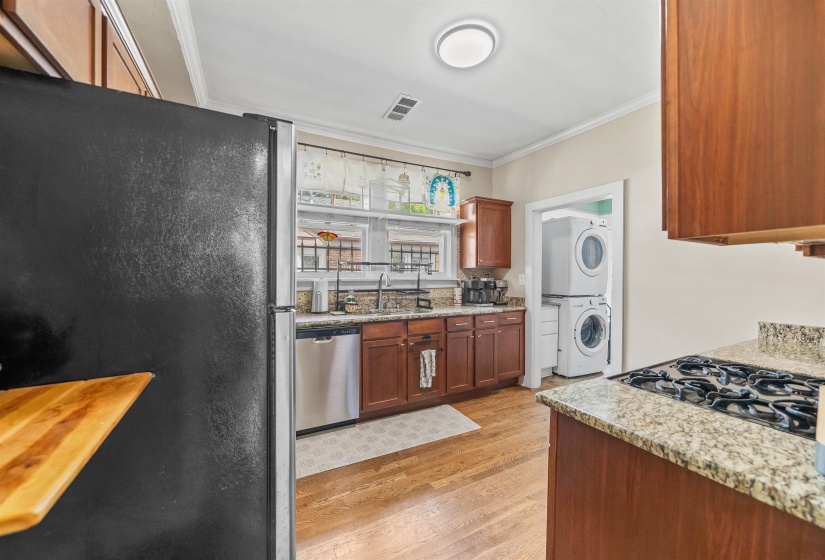 Kitchen with stainless steel appliances, ornamental molding, light wood-type flooring, stacked washer / drying machine, and light stone counters