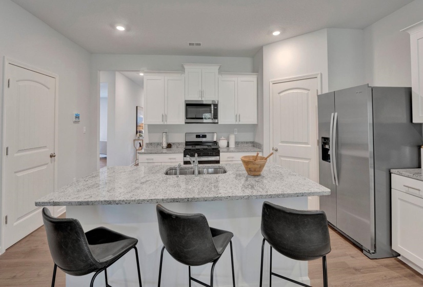 Kitchen featuring stainless steel appliances, white cabinetry, light stone counters, a kitchen island with sink, and recessed lighting