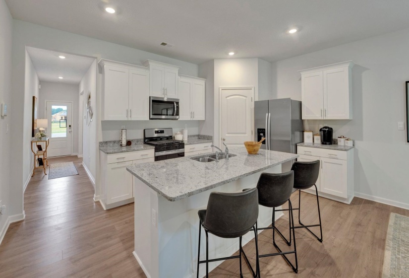 Kitchen featuring white cabinets, stainless steel appliances, light stone counters, a kitchen breakfast bar, and a center island with sink
