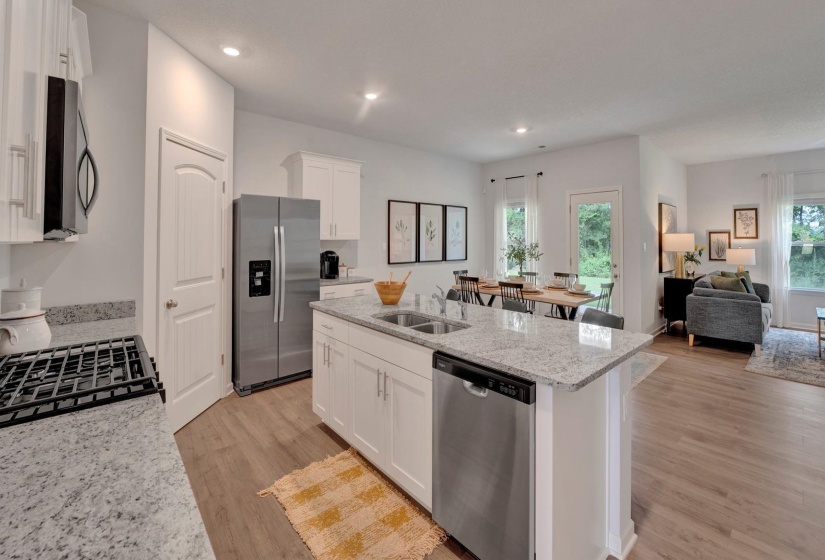 Kitchen with light stone countertops, stainless steel appliances, white cabinets, open floor plan, and an island with sink