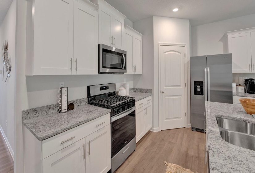 Kitchen featuring stainless steel appliances, white cabinets, light stone countertops, light wood-style floors, and recessed lighting
