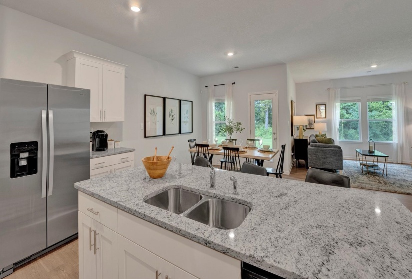 Kitchen featuring light wood-style flooring, stainless steel fridge with ice dispenser, white cabinetry, light stone counters, and healthy amount of natural light