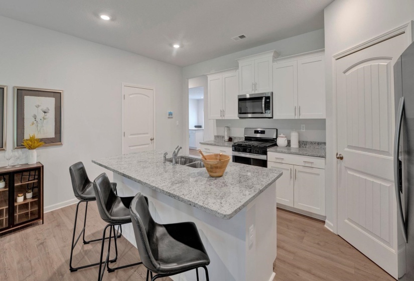 Kitchen with white cabinetry, stainless steel appliances, a center island with sink, a breakfast bar area, and light wood-type flooring