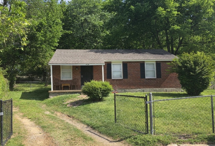 View of front facade with a fenced front yard, a gate, covered porch, brick siding, and a shingled roof