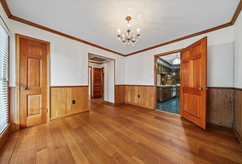Empty room with dark wood-type flooring, ornamental molding, a chandelier, wainscoting, and wooden walls