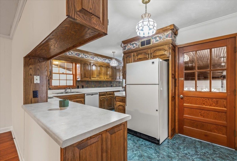 Kitchen featuring pendant lighting, ornamental molding, light countertops, freestanding refrigerator, and brown cabinetry