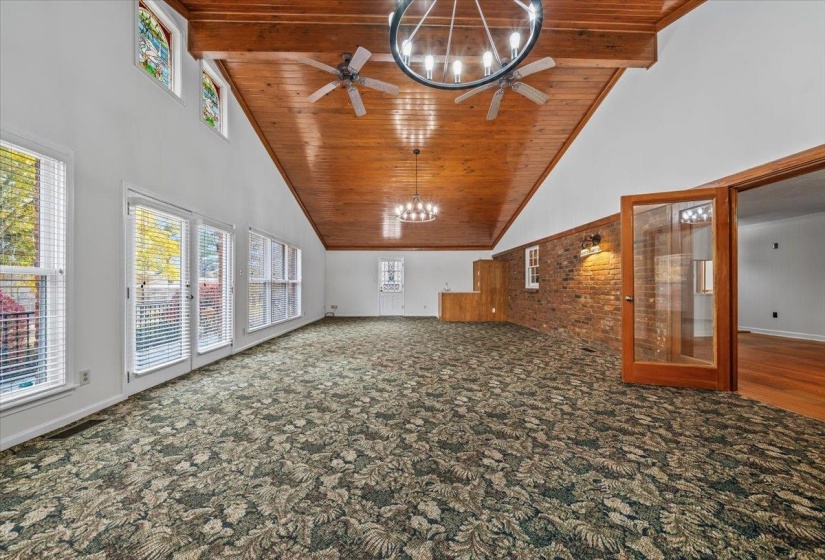 Unfurnished living room with high vaulted ceiling, a wood ceiling with exposed beams, carpet floors, and a chandelier