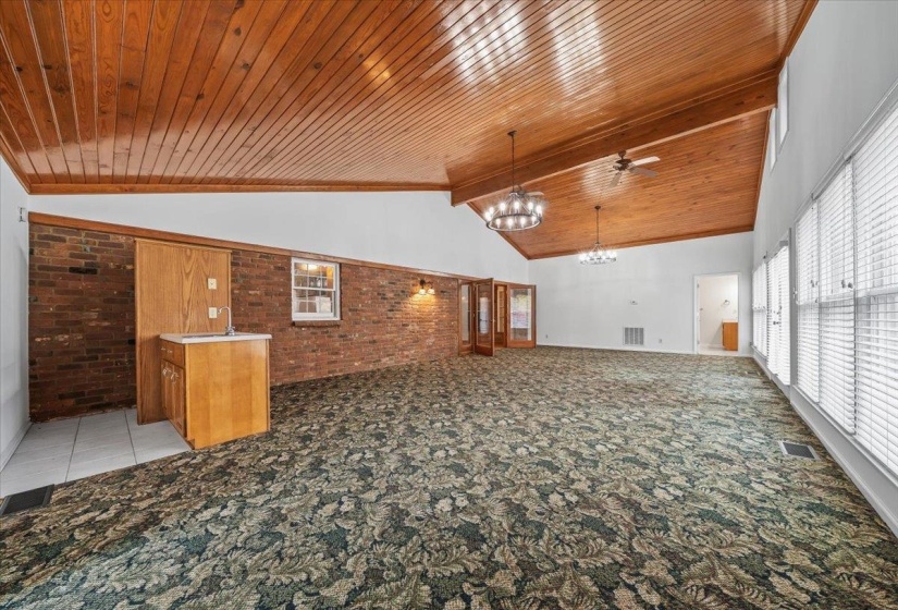 Unfurnished living room with brick wall, light colored carpet, a chandelier, ceiling fan, and a wooden ceiling with exposed beams