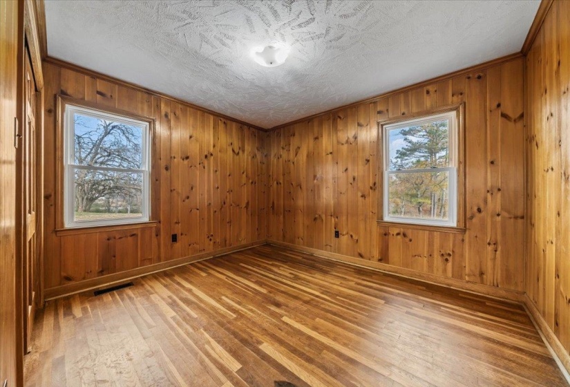 Empty room with wood walls, light wood-type flooring, a textured ceiling, and ornamental molding