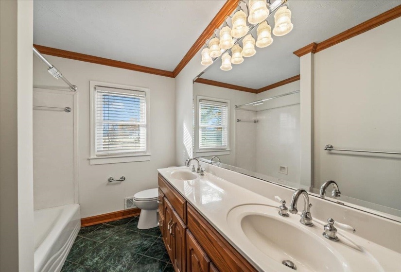 Full bath with double vanity, shower / tub combination, a chandelier, dark tile patterned floors, and crown molding