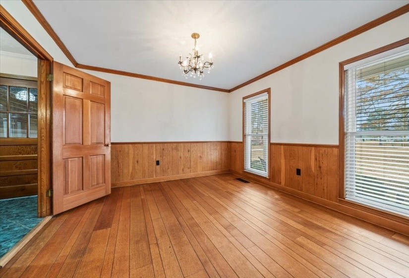 Empty room featuring light wood-type flooring, ornamental molding, a chandelier, a wainscoted wall, and wooden walls