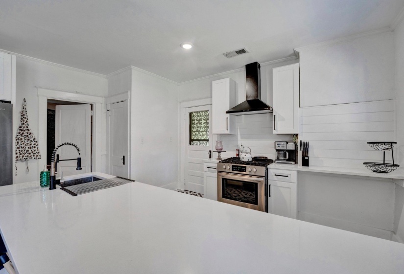 Kitchen featuring stainless steel gas range, white cabinetry, ornamental molding, light stone counters, and recessed lighting