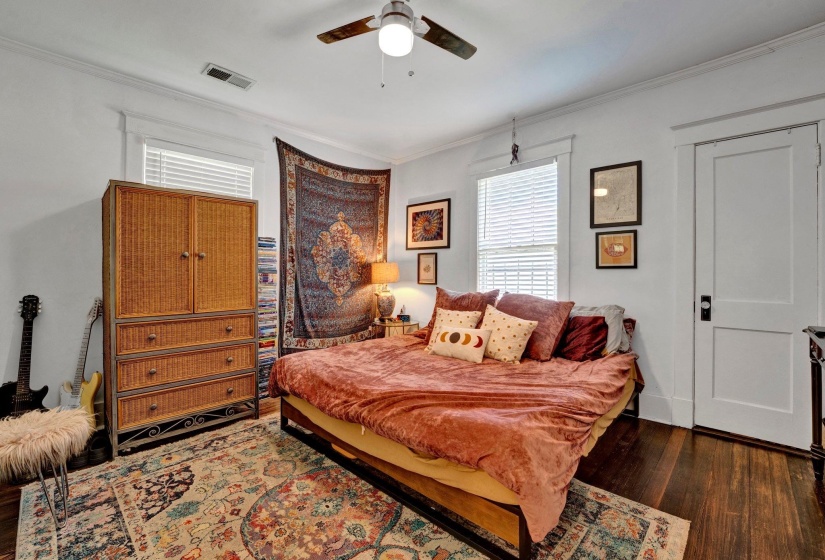 Bedroom featuring dark wood-type flooring, ornamental molding, multiple windows, and a ceiling fan