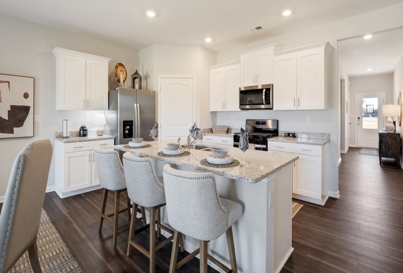 Kitchen with white cabinets, light stone countertops, stainless steel appliances, a kitchen breakfast bar, and a kitchen island with sink