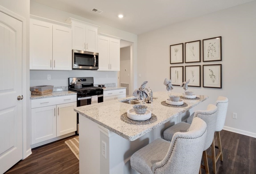 Kitchen featuring white cabinetry, light stone counters, stainless steel appliances, an island with sink, and dark wood-style floors