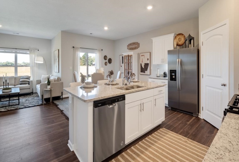 Kitchen with stainless steel appliances, white cabinetry, light stone counters, open floor plan, and an island with sink