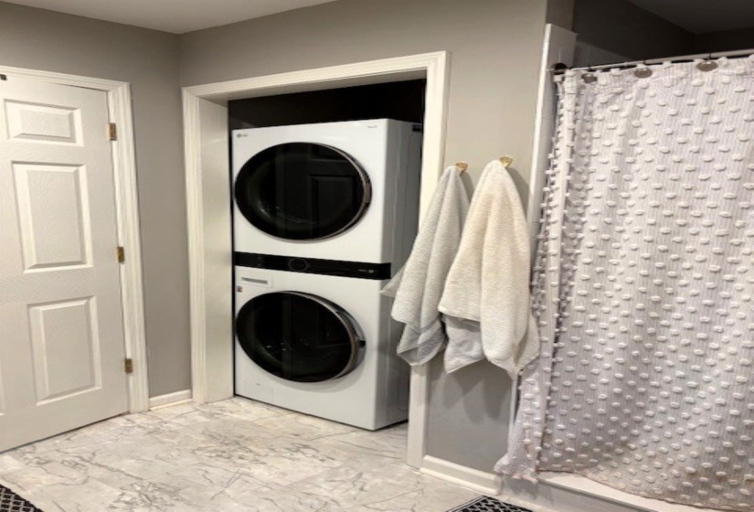 Laundry area with stacked washer and dryer and light marble finish floors